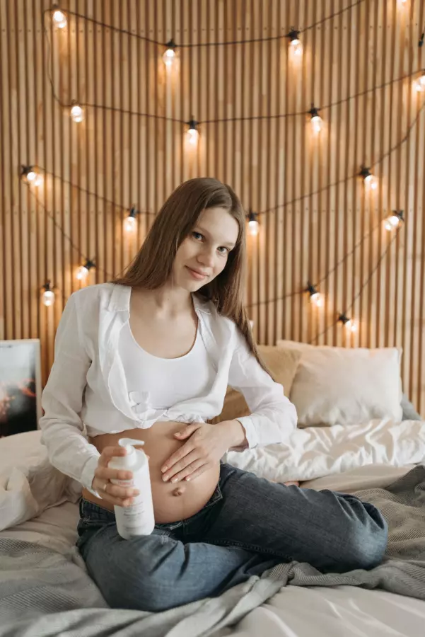 Seorang ibu hamil yang sedang merawat kulit perut selama kehamilan dengan menggunakan krim pelembab
